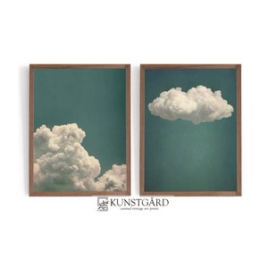 May include: Two framed prints of clouds against a teal blue sky. The prints are in wooden frames with a light brown finish. The text "KUNSTGÅRD curated vintage art prints" is below the prints.