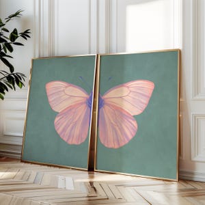 Pode incluir: Duas impressões emolduradas de uma borboleta rosa com detalhes azuis sobre um fundo azul-esverdeado.