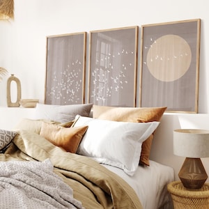 Puede incluir: Tres impresiones enmarcadas con un diseño minimalista que presenta una bandada de pájaros sobre un fondo marrón claro. Las impresiones están colgadas sobre una cama con una funda nórdica de lino beige y una almohada blanca.