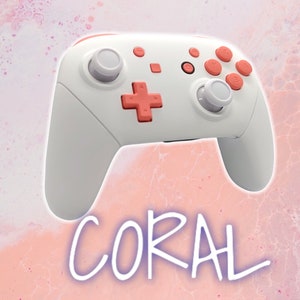May include: A white gaming controller with coral-colored buttons and accents. The controller features a directional pad, analog sticks, and various buttons. The word "CORAL" is written in a stylized font below the controller.
