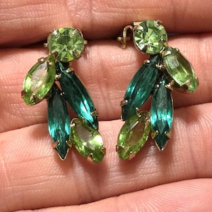 May include: A pair of cluster earrings featuring faceted marquise and round-cut crystals in shades of lime green and deep teal. Each earring is set in a gold-tone metal frame with prong settings, arranged in a leaf-like pattern with a round stone at the top.