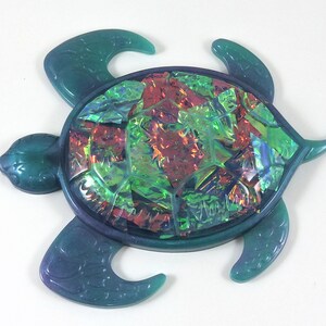 May include: A teal green plastic turtle with a iridescent mosaic shell. The shell is made of small, colorful pieces of glass.