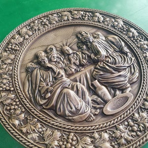 May include: A round wooden plaque with a carved image of the Last Supper. The plaque is decorated with a grapevine border.