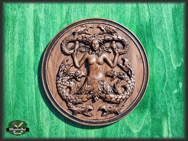 Op de afbeelding: Een houten wandplaquette met daarop een vrouw met slangenhaar, omringd door vier zeeslangen. De plaquette is rond en heeft een donkerbruine afwerking.