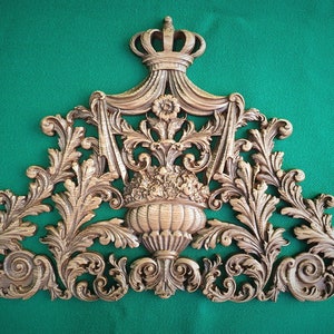 May include: A gold-toned decorative wall plaque with a crown at the top and intricate floral designs. The plaque is shaped like a triangle and has a scalloped edge.