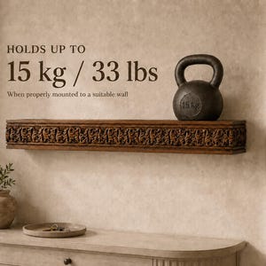 Pu&ograve; includere: Una mensola da parete in legno marrone scuro con intricati motivi floreali intagliati sul bordo anteriore. Il testo sulla parete recita: HOLDS UP TO 15 kg / 33 lbs When properly mounted to a suitable wall. Una kettlebell nera da 15 kg &egrave; appoggiata sopra.