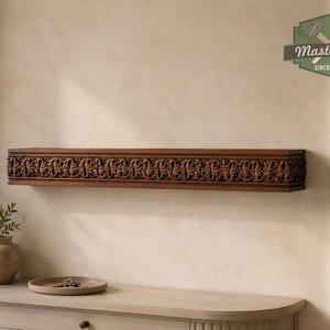 Pu&ograve; includere: Una mensola rettangolare in legno con intricati motivi a foglia intagliati lungo il bordo anteriore. La mensola &egrave; montata a parete e presenta una ricca finitura marrone. Un logo nell'angolo in alto a destra mostra il testo MasterOak SINCE 1998.