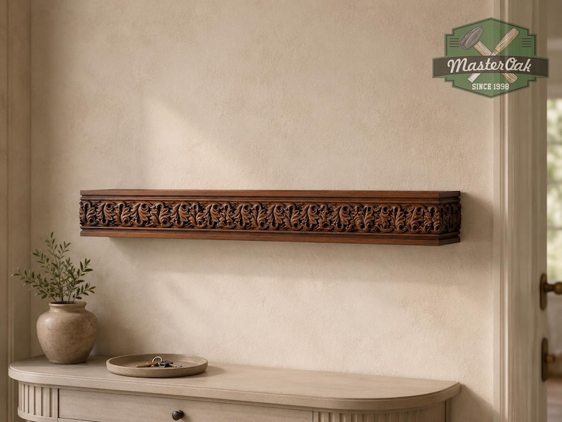 Pu&ograve; includere: Una mensola rettangolare in legno con intricati motivi a foglia intagliati lungo il bordo anteriore. La mensola &egrave; montata a parete e presenta una ricca finitura marrone. Un logo nell'angolo in alto a destra mostra il testo MasterOak SINCE 1998.