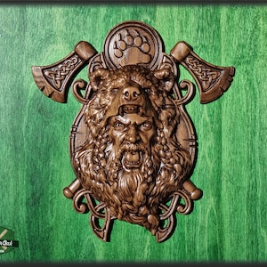 May include: A wooden wall sculpture of a bear's head with a Viking warrior's face, surrounded by two axes and a bear paw print. The sculpture is carved in a dark brown wood and has a detailed design.