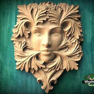 Könnte beinhalten: Eine geschnitzte Holz-Wanddekoration mit einem friedlichen Gesicht, umgeben von detailliertem Blattwerk. Die natürlichen Holztöne und die aufwendige Schnitzerei erzeugen einen beeindruckenden 3D-Effekt. Auf einer türkisgrünen Holzoberfläche montiert.