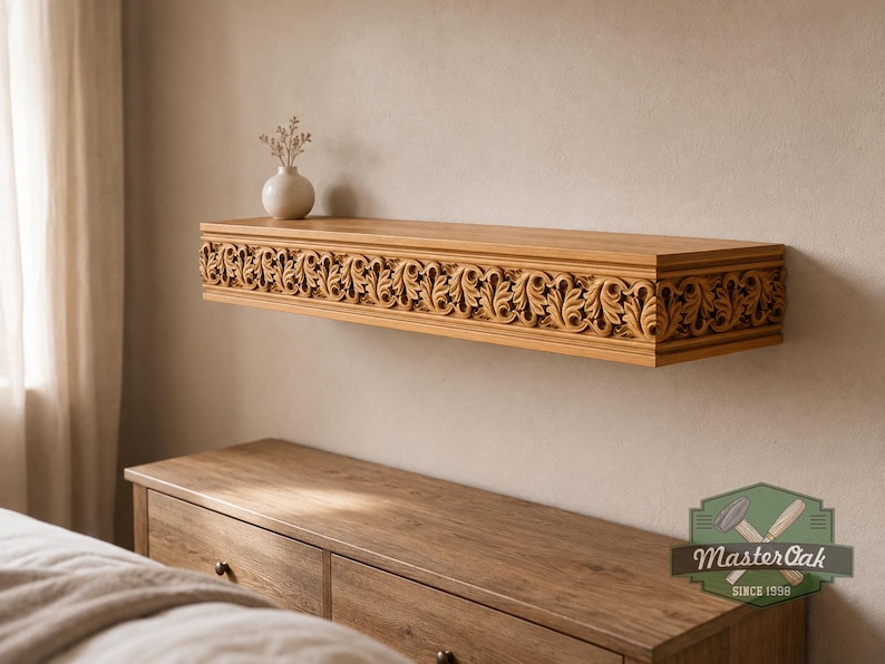 Pu&ograve; includere: Una mensola galleggiante in legno marrone chiaro con un intricato motivo a foglie intagliate sul bordo anteriore. Un piccolo vaso bianco con fiori secchi si trova sul lato sinistro. Il testo MasterOak SINCE 1998 &egrave; visibile nell'angolo in basso a destra.