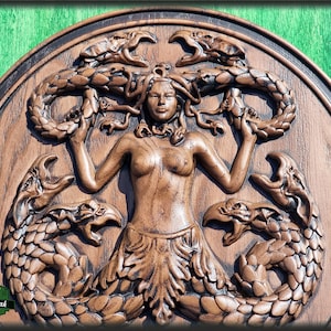 Op de afbeelding: Een houten wandplaquette met een gedetailleerde houtsnijwerk van Medusa, een mythische Griekse figuur met slangenhaar, omringd door slangen en griffioenen. De plaquette is in een donkerbruine kleur gebeitst.