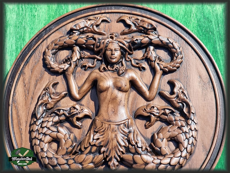 Op de afbeelding: Een houten wandplaquette met een gedetailleerde houtsnijwerk van Medusa, een mythische Griekse figuur met slangenhaar, omringd door slangen en griffioenen. De plaquette is in een donkerbruine kleur gebeitst.
