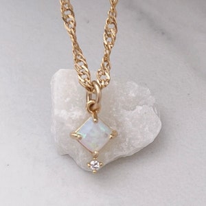 May include: Two gold necklaces with opal and diamond pendants on white stone bases.