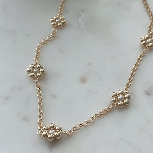 May include: A gold chain necklace with five flower-shaped charms. Each charm is made of small gold beads and has a single white pearl in the centre.