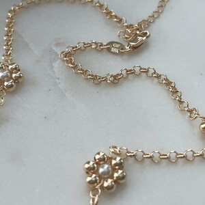 May include: A gold chain necklace with small flower charms. Each flower charm has a pearl in the centre. The chain has a clasp with the inscription "GF 18K".