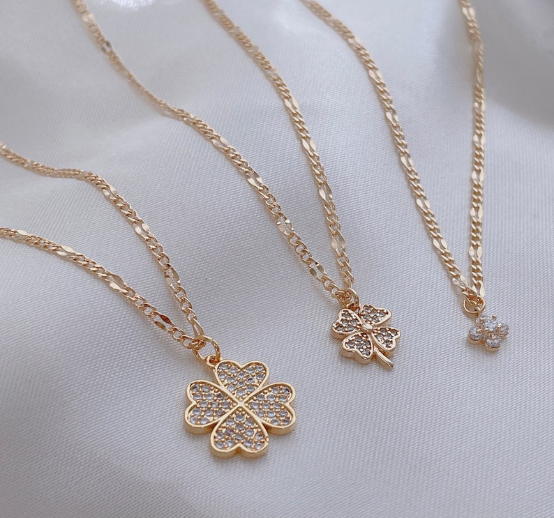 May include: Three gold necklaces with four-leaf clover pendants. The pendants are adorned with sparkling clear rhinestones.