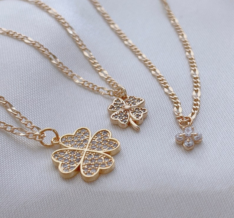 May include: Three gold necklaces with four-leaf clover pendants adorned with clear cubic zirconia stones. The necklaces feature different chain styles.
