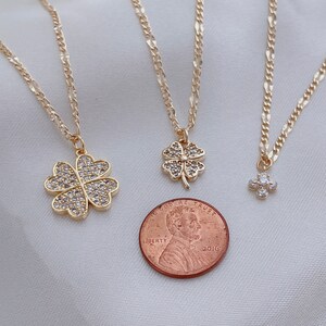 May include: Three gold necklaces with four-leaf clover pendants adorned with clear cubic zirconia stones. The largest pendant is about the size of a US penny.