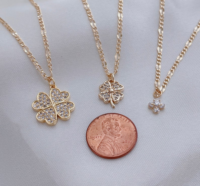 May include: Three gold necklaces with four-leaf clover pendants adorned with clear cubic zirconia stones. The largest pendant is about the size of a US penny.
