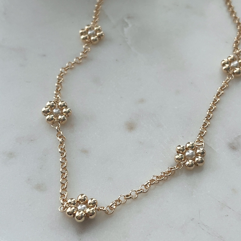 May include: A gold chain necklace with five flower-shaped charms. Each charm is made of small gold beads and has a single white pearl in the centre.