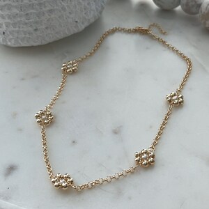 May include: A gold chain necklace with five flower-shaped charms. Each charm is made of small gold beads and has a single white pearl in the centre.