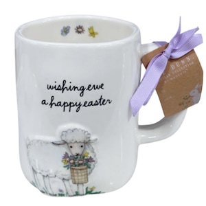 May include: White ceramic mug with a sheep illustration carrying a basket of flowers. The mug has the text "wishing ewe a happy easter". A lavender ribbon and a tag are attached to the handle. The mug is part of the Dunn Easter Collection.