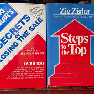 Puede incluir: Dos libros de tapa dura de Zig Ziglar. El libro de la izquierda se titula "Secrets of Closing the Sale" con una portada roja y blanca. El libro de la derecha se titula "Steps to the Top" con una portada roja, blanca y azul.