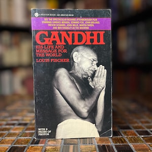 May include: A vintage paperback book titled "Gandhi: His Life and Message for the World" by Louis Fischer. The cover features a black and white image of Mahatma Gandhi with his hands together. The book has a purple banner with the film's cast.