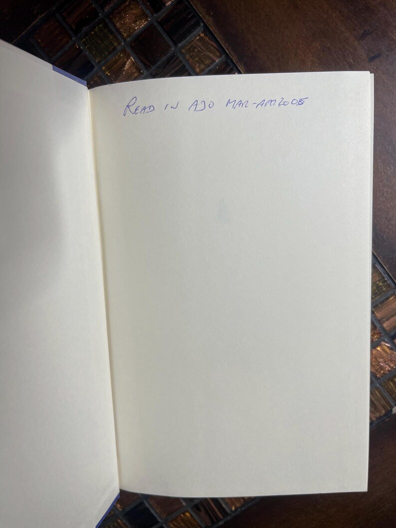 Może przedstawiać: Otwarta książka z pustymi stronami i odręcznym tekstem "Read in Ajo Mar-Am 2005" w niebieskim atramencie. Strony książki są w kolorze złamanej bieli, a oprawa jest widoczna. Tło to ciemna, wzorzysta powierzchnia.