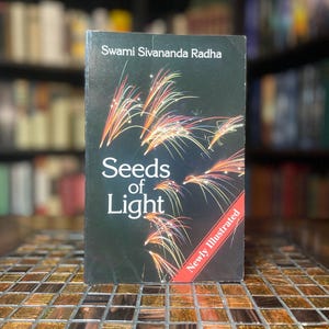 May include: A book titled "Seeds of Light" by Swami Sivananda Radha. The cover is dark with a colorful illustration of fireworks. The words "Seeds of Light" are in white. A red banner reads "Newly Illustrated".