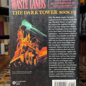 May include: The back cover of "The Waste Lands," Book III of The Dark Tower series by Stephen King. The cover features a vibrant illustration of a train with a green, smoky effect. Text includes the title, author, and a summary of the book.