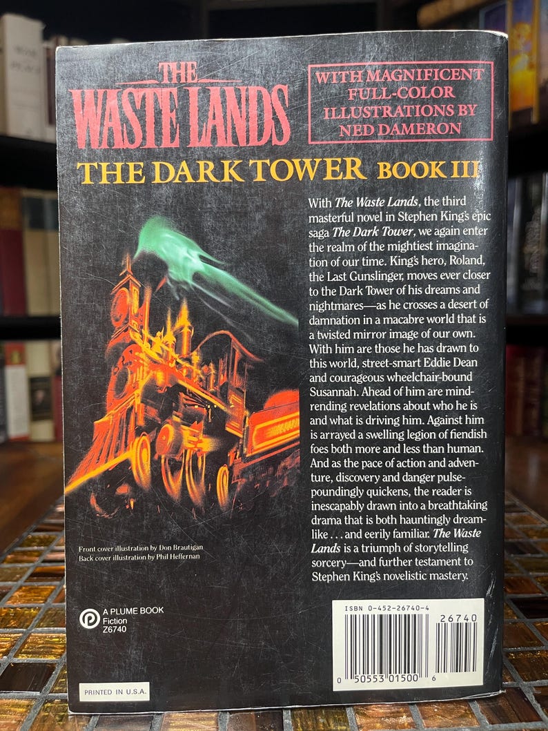 May include: The back cover of "The Waste Lands," Book III of The Dark Tower series by Stephen King. The cover features a vibrant illustration of a train with a green, smoky effect. Text includes the title, author, and a summary of the book.