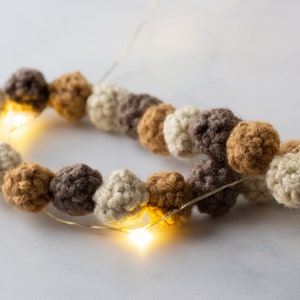 Puede incluir: Una guirnalda de bolas de crochet en color beige, marr&oacute;n y tostado con una hebra de luces de hadas tejida a trav&eacute;s de ellas.