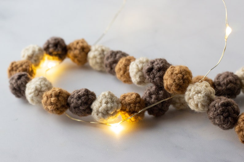 Puede incluir: Una guirnalda de bolas de crochet en color beige, marr&oacute;n y tostado con una hebra de luces de hadas tejida a trav&eacute;s de ellas.
