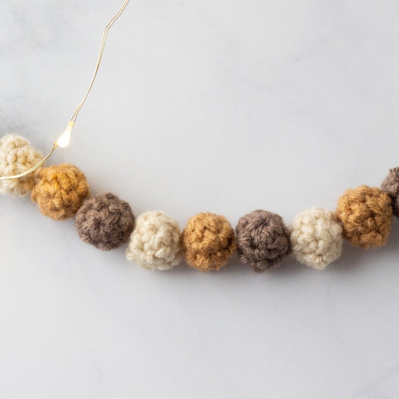 Puede incluir: Una guirnalda de bolas de crochet en tonos beige, marr&oacute;n y dorado. Las bolas est&aacute;n enhebradas con un fino alambre dorado.