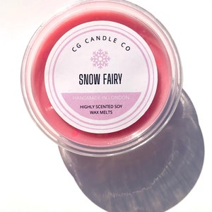 May include: A small pink wax melt container with a white label that reads "CG Candle Co. Snow Fairy Handmade in London Highly Scented Soy Wax Melts".