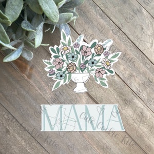 May include: A white sticker with a floral arrangement in a vase and the word "MAMA" in a blue font.