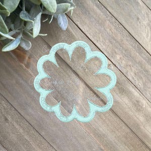 May include: A light blue plastic cookie cutter shaped like a flower with five petals. The cutter has the words "Daisy Cookie Cutters" written around the edge.
