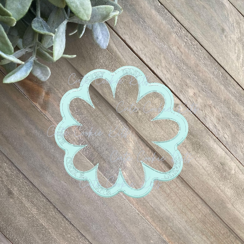 May include: A light blue plastic cookie cutter shaped like a flower with five petals. The cutter has the words "Daisy Cookie Cutters" written around the edge.
