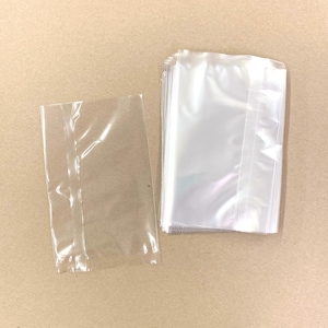 Pode incluir: Uma pilha de sacos de plástico transparentes com um único saco deitado sobre uma superfície castanha. Os sacos são todos do mesmo tamanho e têm uma abertura selada a quente.