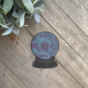 May include: A blue and purple glass snow globe with white stars and a swirling design inside. The snow globe is on a black base with a dotted border.