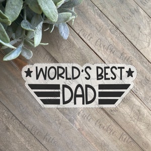 May include: A black and white graphic design with a star on each side and a wing design behind the text "WORLD'S BEST DAD".