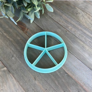 May include: A light blue plastic circle cutter with six sections. The cutter is labeled "SIMPLY COOKIE KITS".