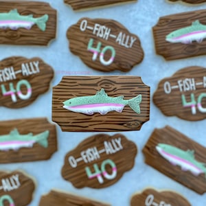 May include: A set of decorated sugar cookies with a woodgrain design. The cookies feature a trout fish and the text "O-FISH-ALLY 40".