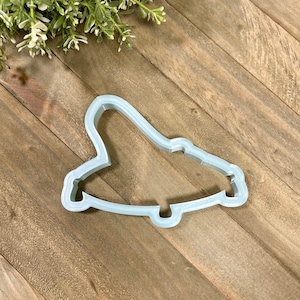 May include: A light gray plastic cookie cutter shaped like a vintage car. The cutter is on a wooden surface.