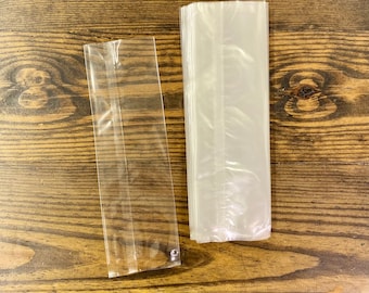Puede incluir: Dos bolsas de plástico transparentes, una es más alta y ancha que la otra. Ambas bolsas están puestas planas sobre una superficie de madera.