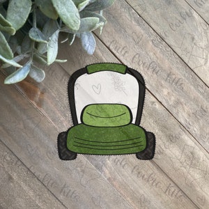 May include: Green lawnmower cookie cutter with a black outline. The cutter is shaped like a riding lawnmower with a seat and wheels.