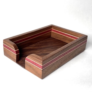May include: A rectangular wooden desk organizer with a dark brown finish. The organizer features a red stripe and a lighter wood accent. The design includes a curved front opening for easy access. The overall aesthetic is modern and minimalist.