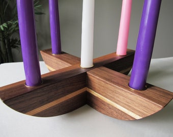 May include: A wooden candle holder with four purple candles, one white candle, and one pink candle. The holder is made of dark brown wood with a lighter wood accent. The candles are arranged in a cross shape.